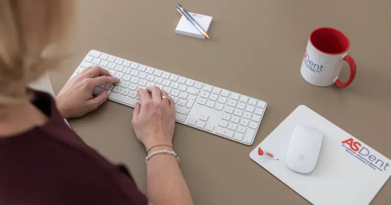 Hände an der Tastatur neben ASDent-Tasse und Mauspad – Vor- und Nachteile der externen Abrechnung für Zahnarztpraxen